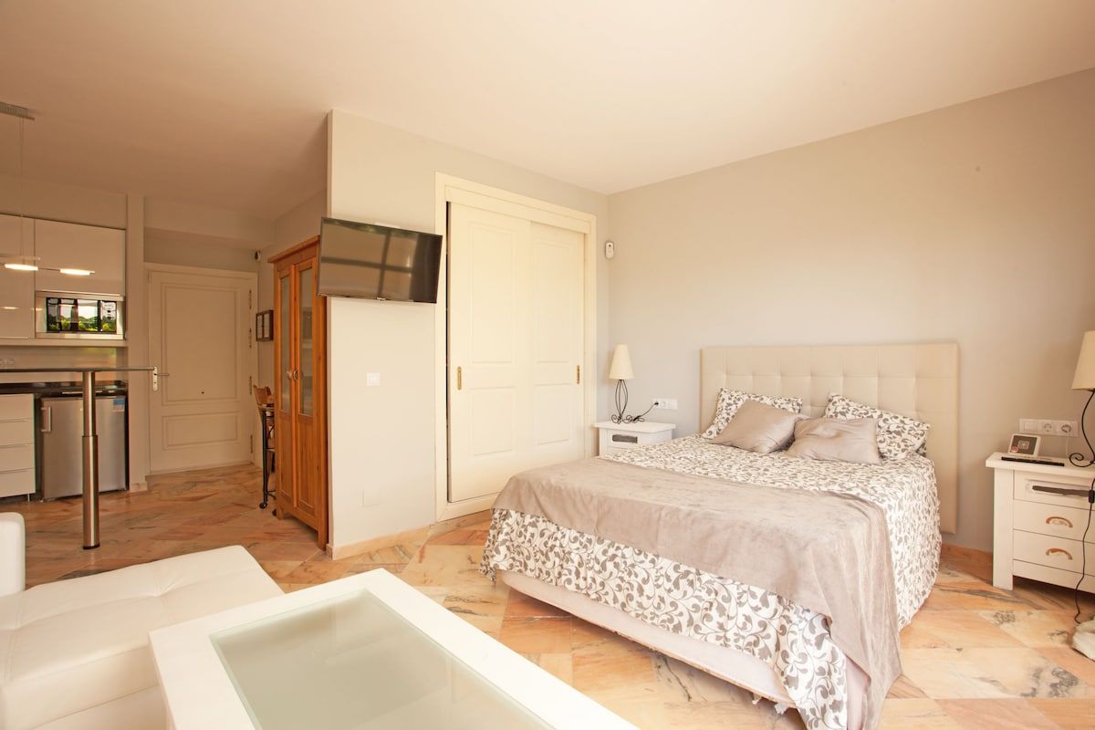 A bedroom with a bed, bedside tables, a TV, and a bathroom with a bathtub.