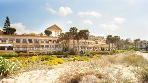 Ein Hotel an der Küste mit mehreren Balkonen, einem sandigen Strand und einer Vielzahl tropischer Pflanzen.