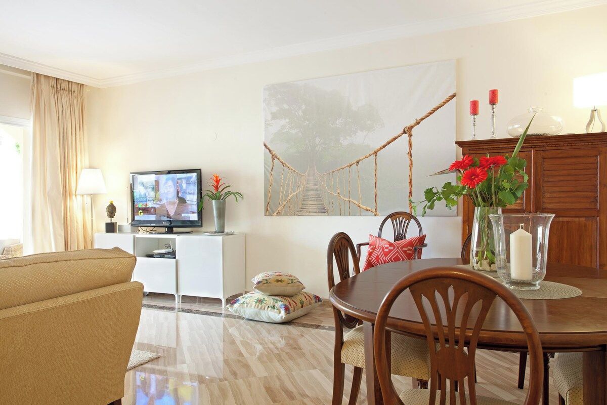 A living room with a television, a dining table with chairs, a sofa, a painting, and a cabinet.