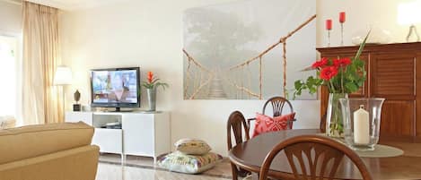 A living room with a television, a dining table with chairs, a sofa, a painting, and a cabinet.