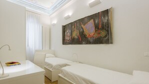 Une chambre d’hôtel moderne, équipée de deux lits simples, d’un bureau avec une lampe et d’un grand tableau abstrait accroché au mur.