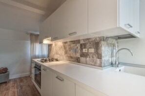 Cocina moderna con gabinetes blancos, salpicadero de mármol, pileta de acero inoxidable y horno integrado.
