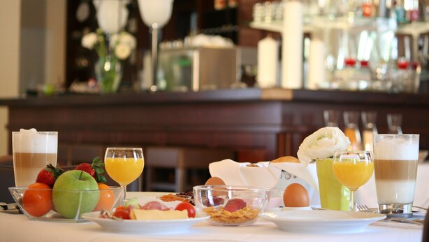 Una mesa de desayuno con diversos alimentos y bebidas, una barra al fondo y una flor sobre la mesa.