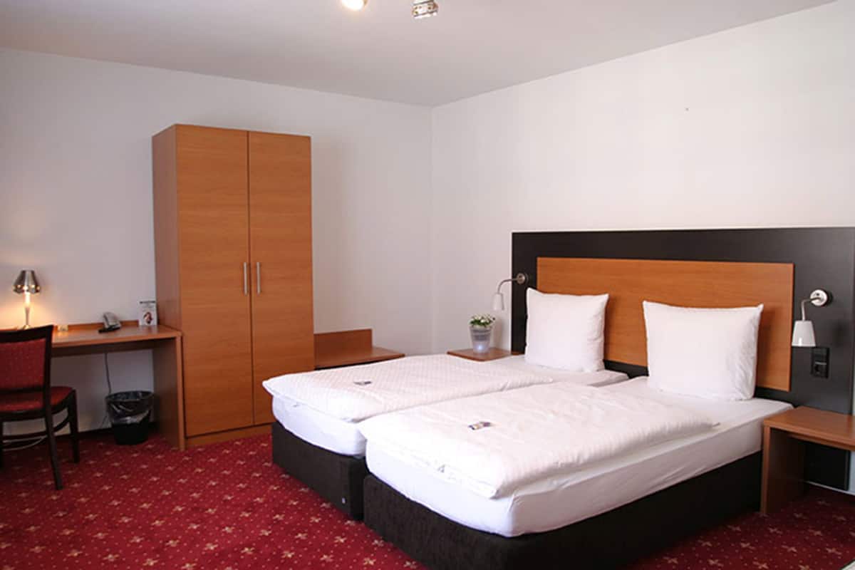 A hotel room with two beds, a desk, a chair, and a wardrobe.