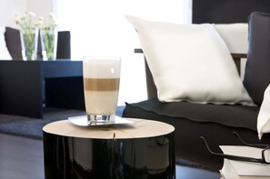 A glass of coffee on a round black table with a white cushion and a black sofa in the background. - Hotel zum Rössel (Kandel)