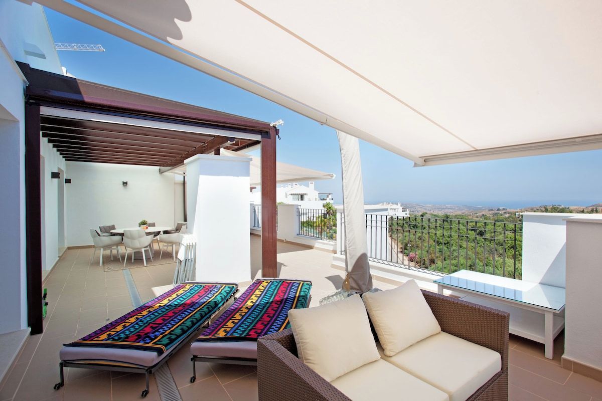 A balcony with a view, a dining area, and a lounge with a colorful bedspread.