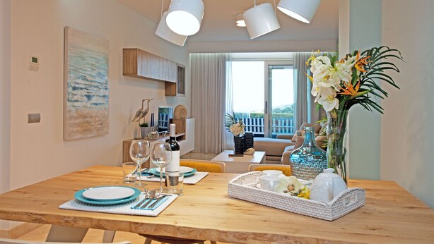 A dining area with a wooden table set for four, a vase with flowers, and a view of the living room and balcony. - Modern Three bed ground floor apartment La Mairena (Ojen)