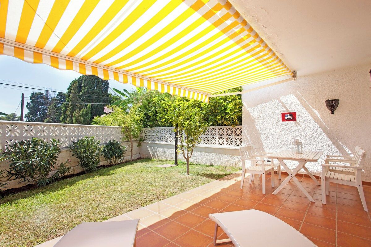 A patio with a striped awning, white outdoor furniture, and a white fence.