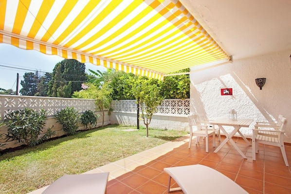 A patio with a striped awning, white outdoor furniture, and a white fence.