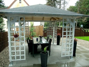 A covered patio area with a table and chairs, surrounded by a white lattice structure.