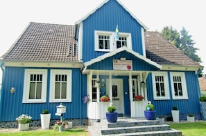 A blue house with a tiled roof, a porch with potted plants, and a sign indicating it is a bed and breakfast.