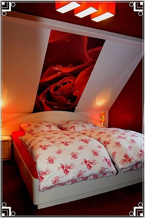 A bedroom with a bed, floral bedding, a nightstand, and a wall-mounted light.