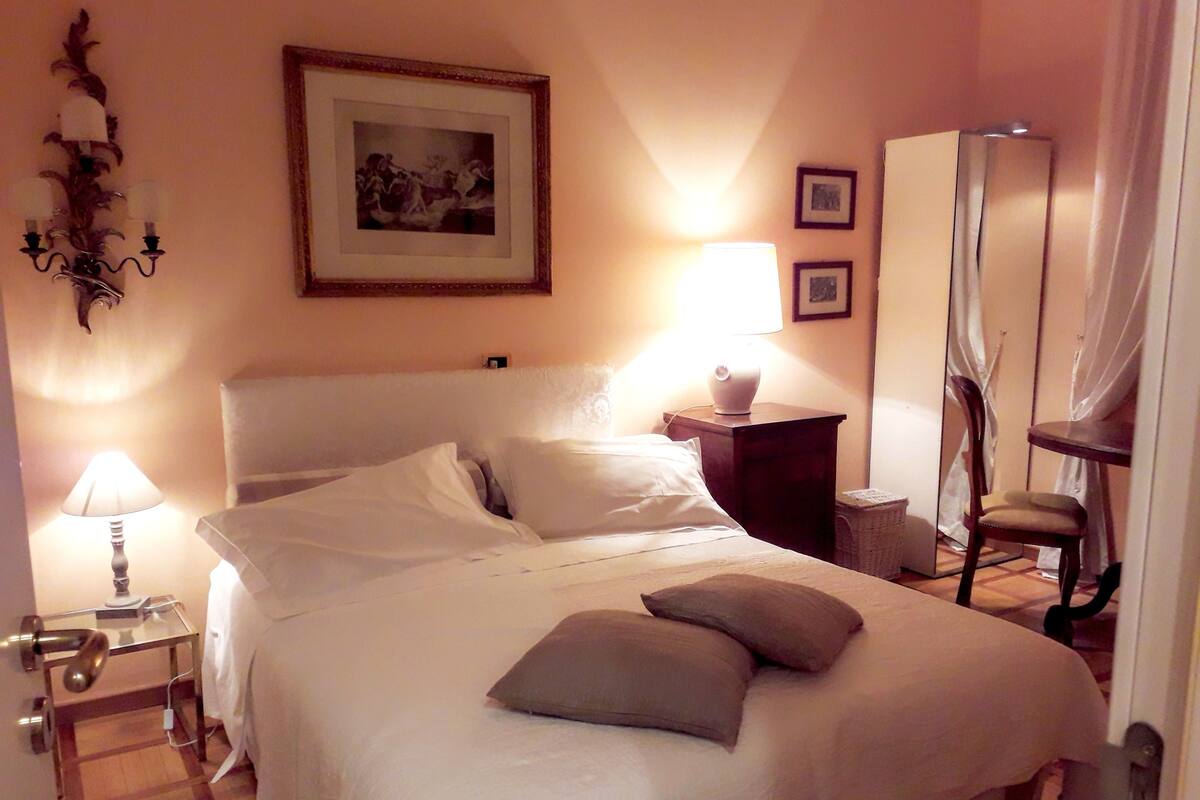 A hotel room with a bed, bedside lamps, a framed picture on the wall, a mirror, and a chair.
