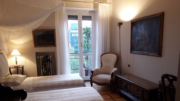A bedroom with two beds, a chair, a desk, a lamp, and a painting. - Light Charme (Milan)
