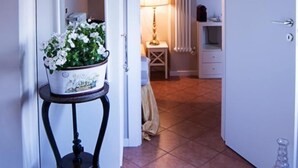 A hallway with a white door, a small table with a potted plant, a lamp, and a radiator. - Light Charme (Milan)
