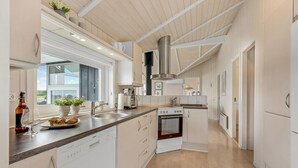 Una cocina moderna con lavavajillas Bosch, una campana extractora de acero inoxidable y un amplio ventanal que proporciona luz natural.
