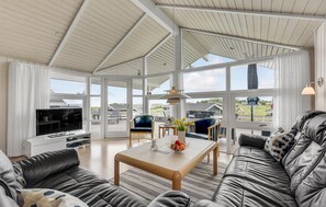 Relax in a spacious living area with expansive views of the surrounding landscape, featuring a comfortable seating arrangement and a large television.