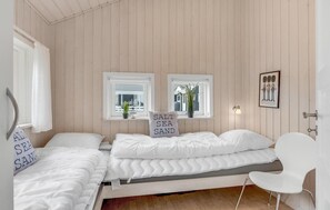 Two single beds with coastal-themed pillows, a potted plant, and a framed picture adorn this inviting bedroom.