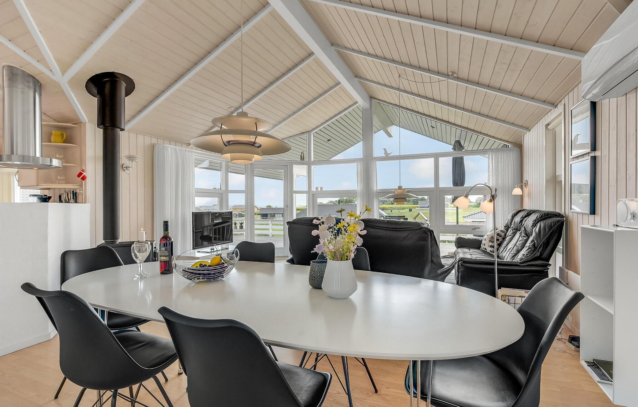 A dining area with a round table, black chairs, and a view of the outdoors through large windows.