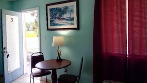 Une pièce aux murs de couleur turquoise, avec un tableau encadré représentant une scène de plage, une table avec deux chaises, une lampe et un rideau rouge.