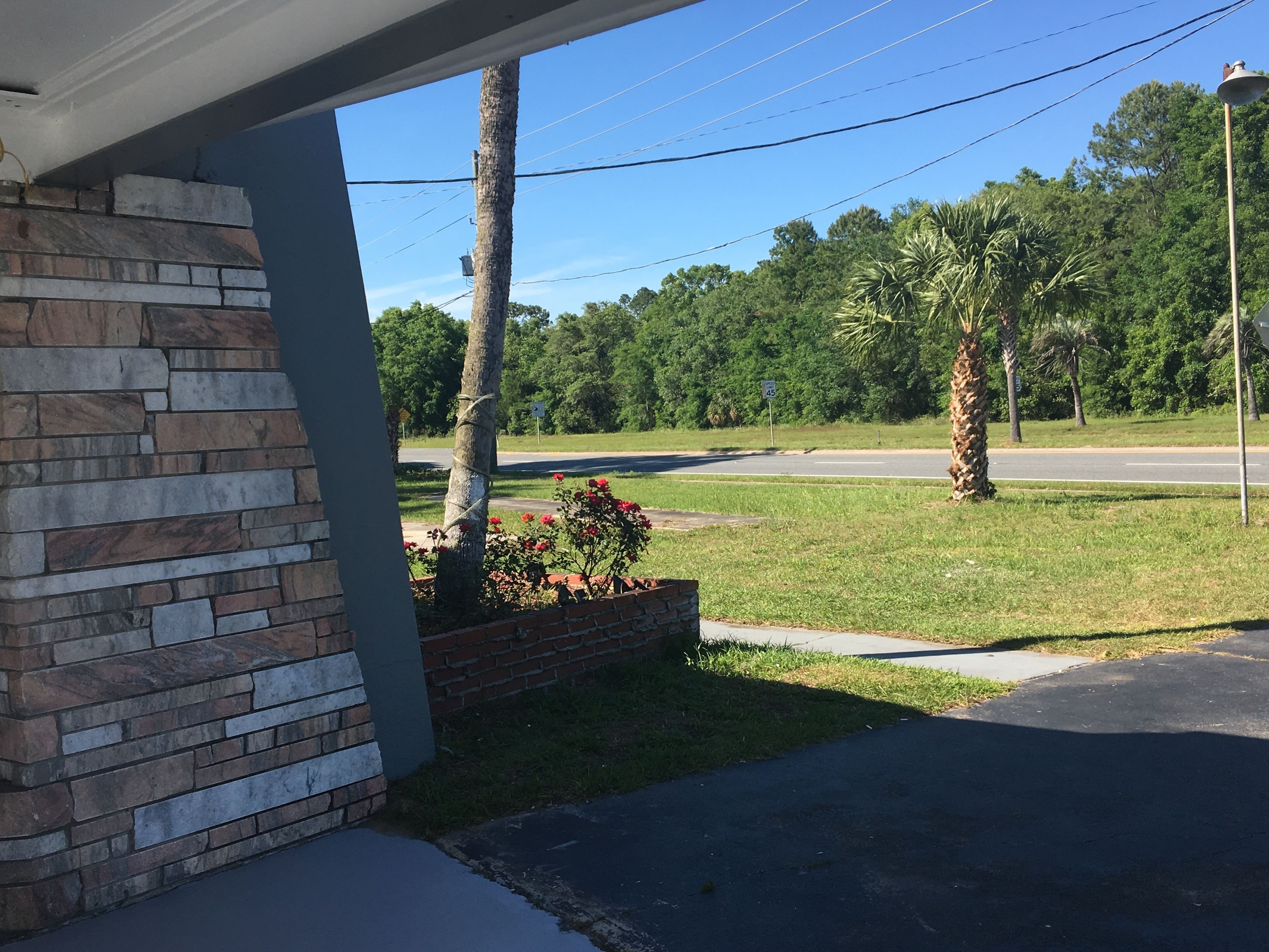 A residential area with a stone facade, a paved driveway, and a road with a speed limit sign.