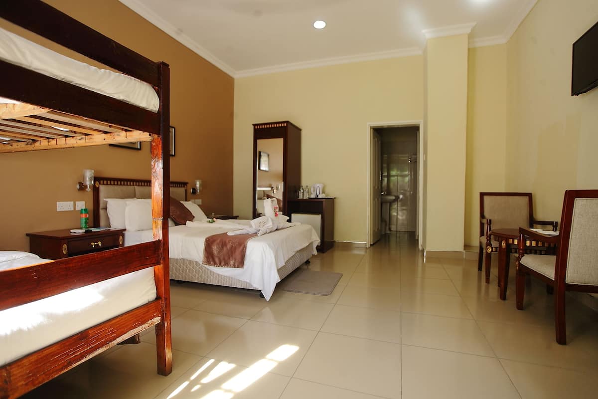 Quarto de hotel com beliche, uma cama de solteiro, banheiro com espelho e área de estar com cadeiras.