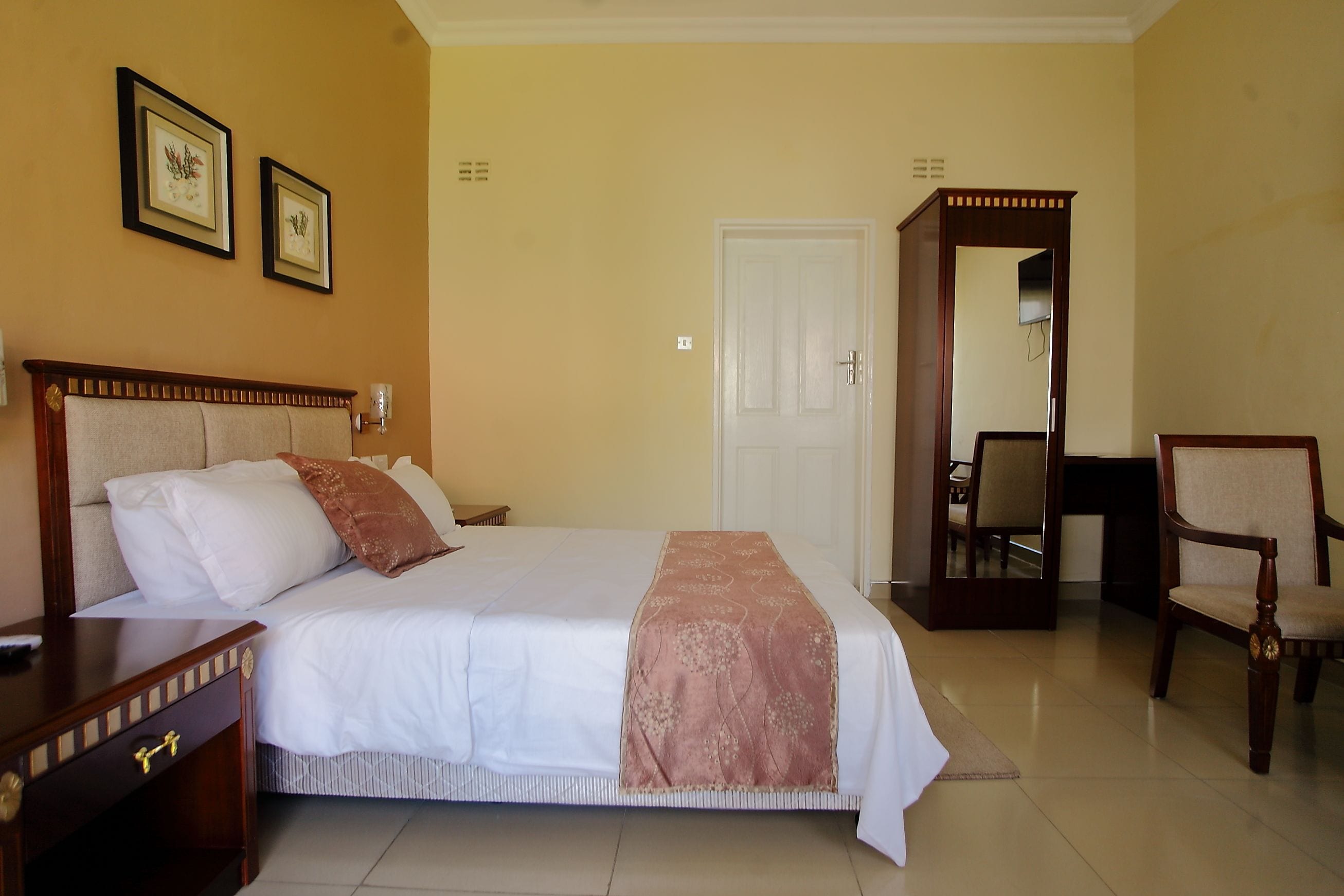 A neatly arranged hotel room with a large bed, a wooden nightstand, a chair, and a door leading to another room.