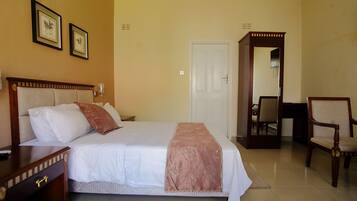 A neatly arranged hotel room with a large bed, a wooden nightstand, a chair, and a door leading to another room.