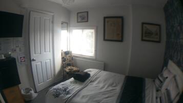 A bedroom with a bed, a chair, a radiator, a window, and a door.