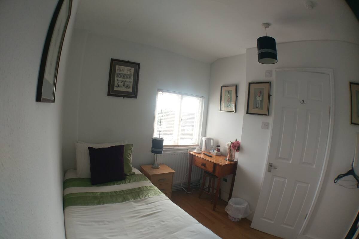 A bedroom with a bed, a desk, a window, and a door.
