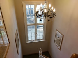 Una escalera con candelabro, un ventanal con vistas y cuadros enmarcados en las paredes.