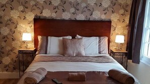 Un lit bien fait, avec une tête de lit, deux lampes de chevet et une télécommande posée sur une serviette marron.