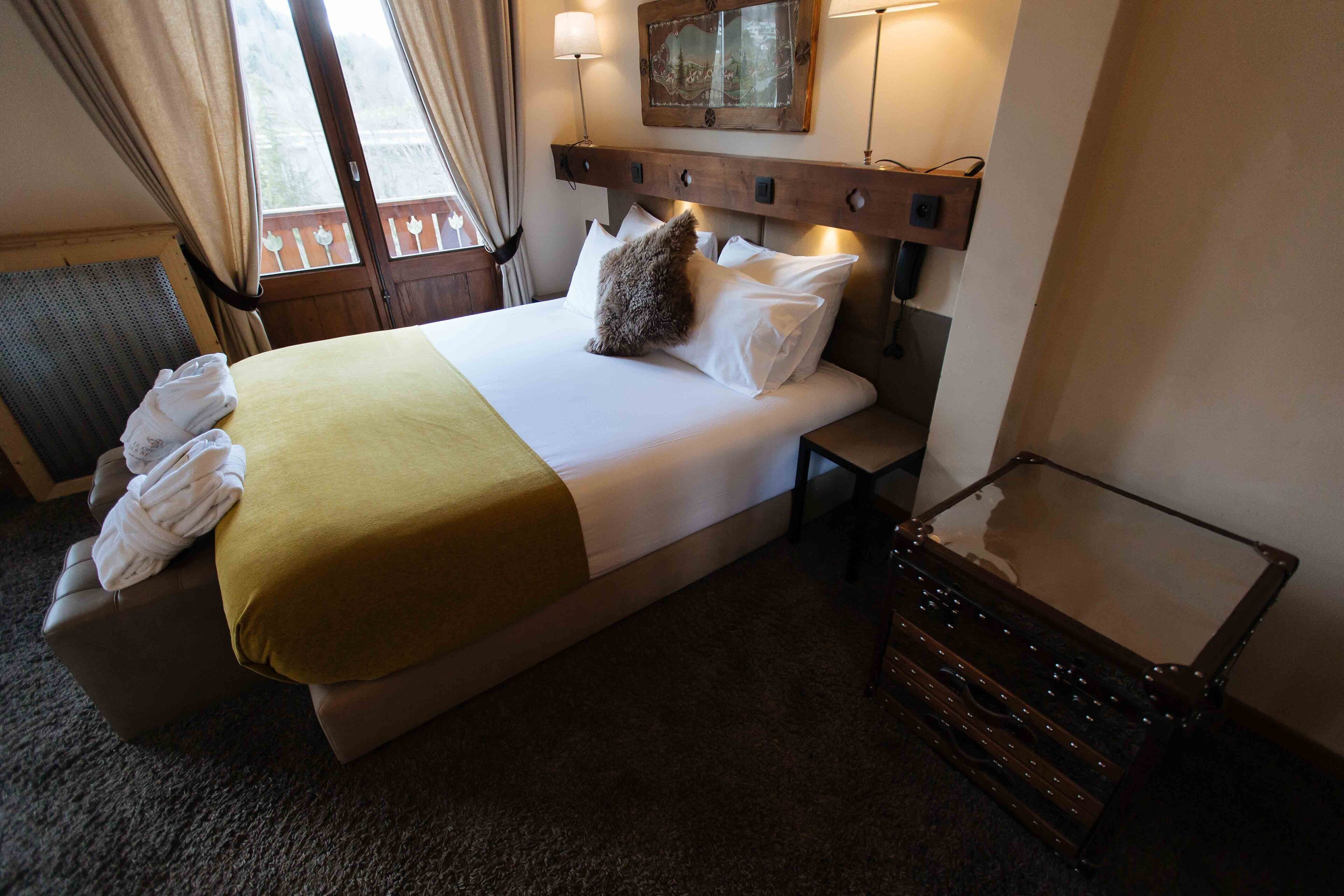 Una habitación de hotel con cama, mesita de noche, espejo y ventana con cortinas.
