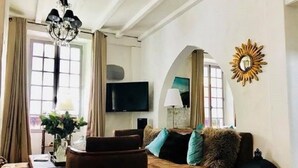 A living room with a brown sofa, a coffee table, a TV, and a chandelier. - Hôtel Le Coeur des Neiges (Saint-Gervais-les-Bains)