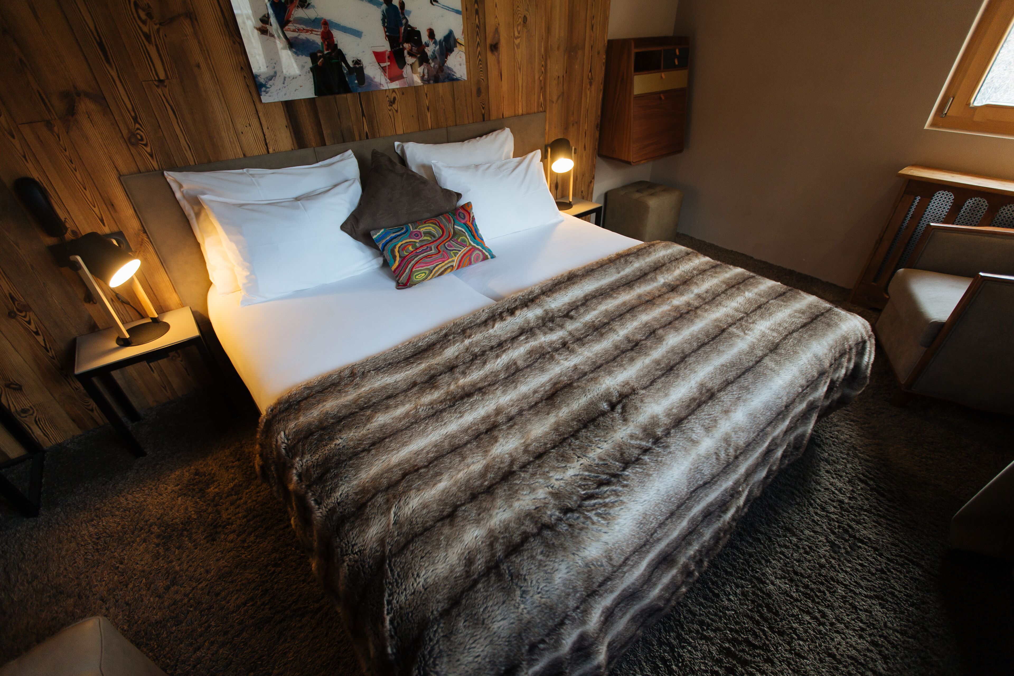 Una cama bien hecha con un edredón a rayas, una almohada colorida y dos lámparas de noche.