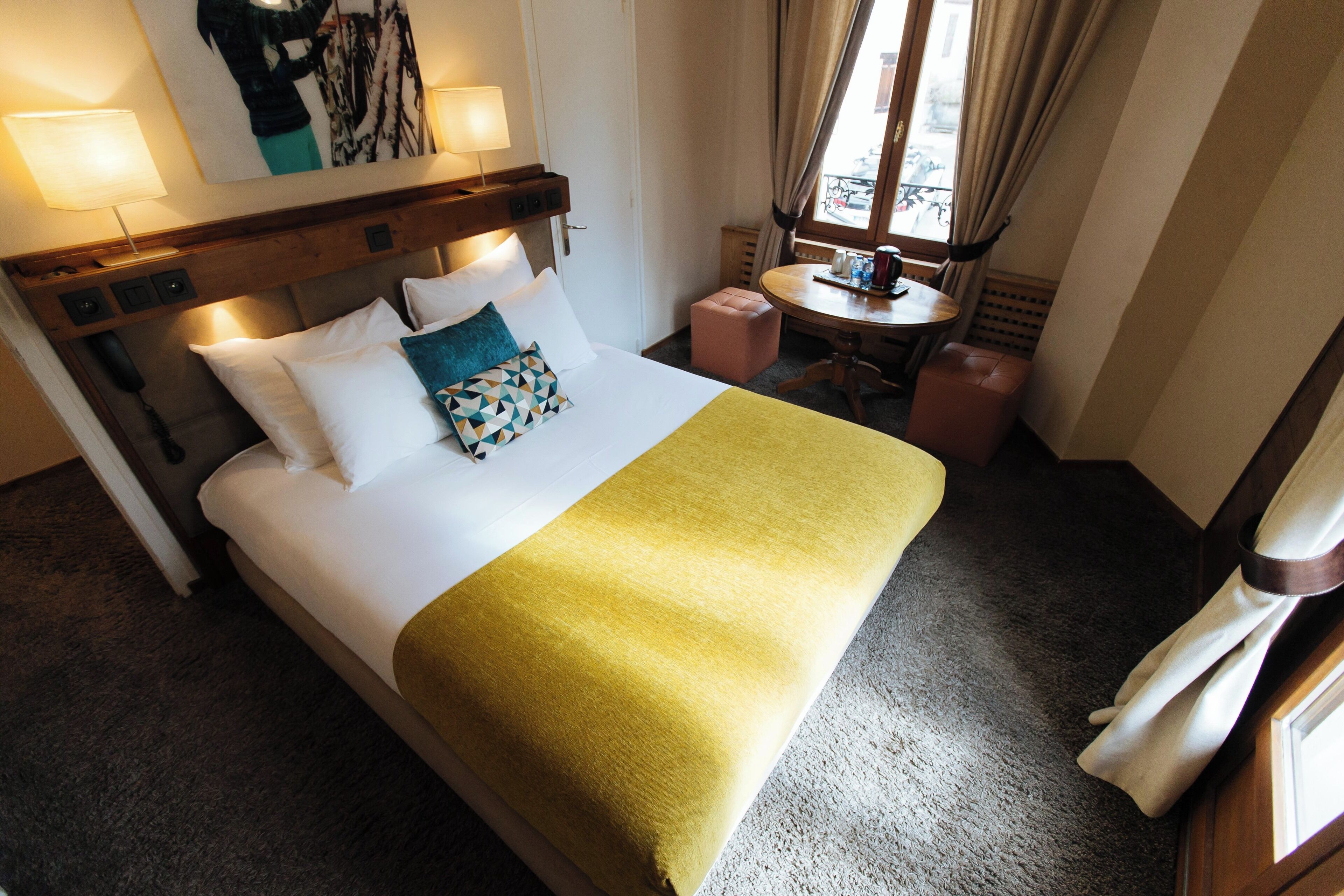 Una habitación de hotel con una cama grande, una mesita pequeña y un ventanal con cortinas.
