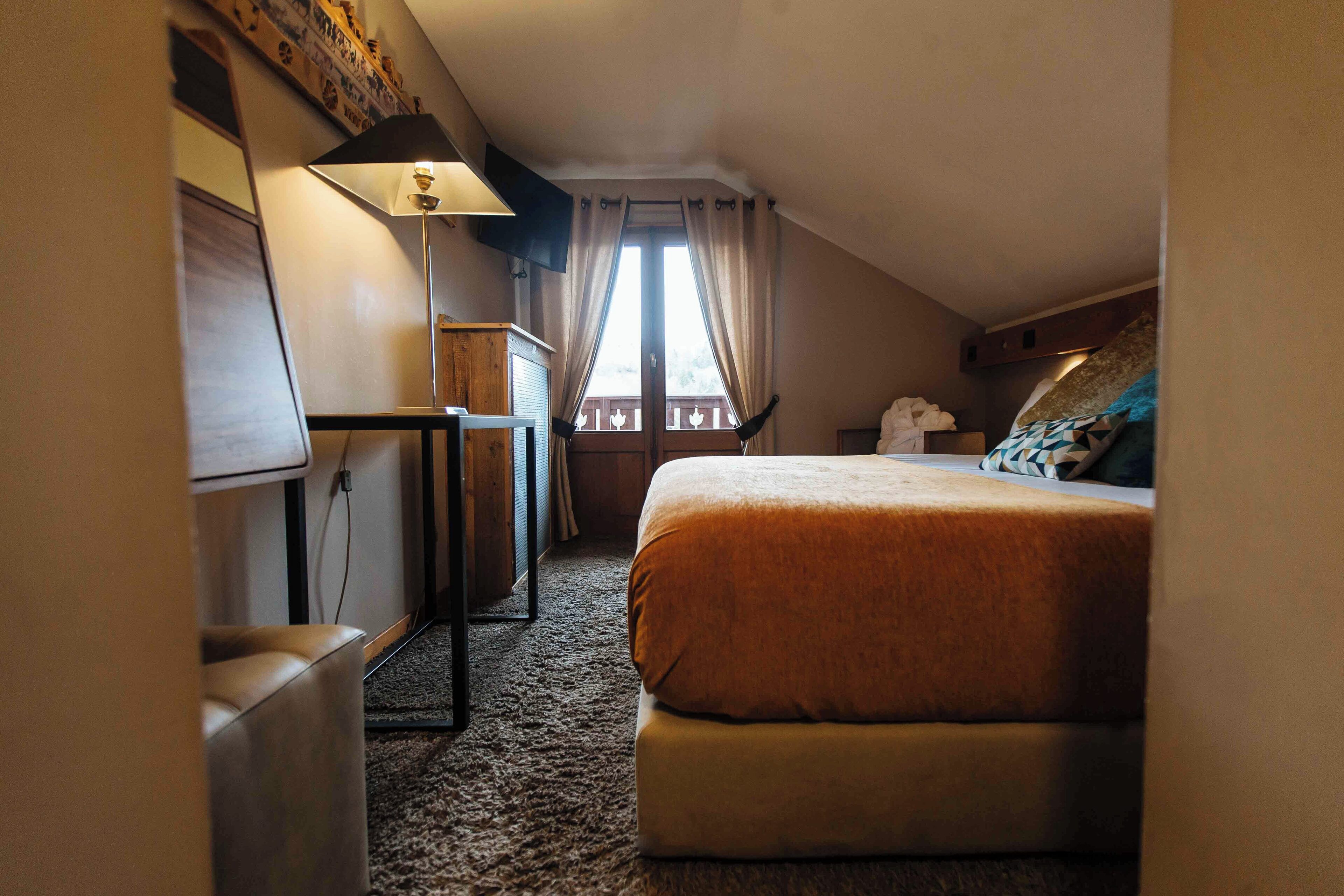 Una habitación de hotel con cama, escritorio, lámpara y ventana con cortinas.