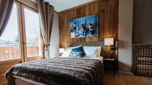 A bedroom with a wooden headboard, a large window with curtains, a painting of skiers, and a fur throw on the bed. - Hôtel Le Coeur des Neiges (Saint-Gervais-les-Bains)