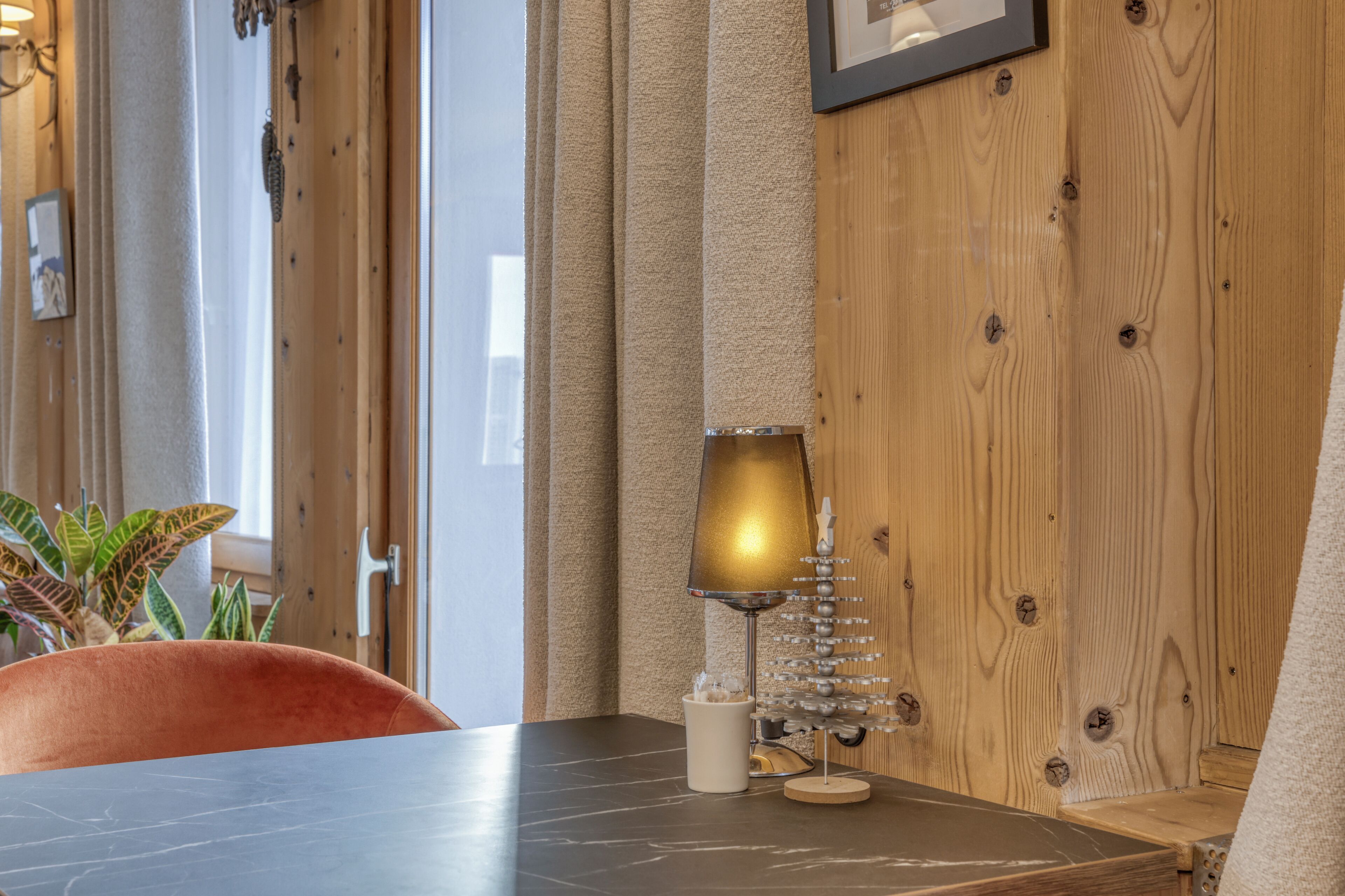 Una pared de madera con un cuadro enmarcado, una mesa con una lámpara y una planta.
