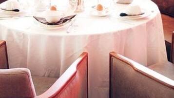 A round dining table with a white tablecloth, surrounded by cushioned chairs.