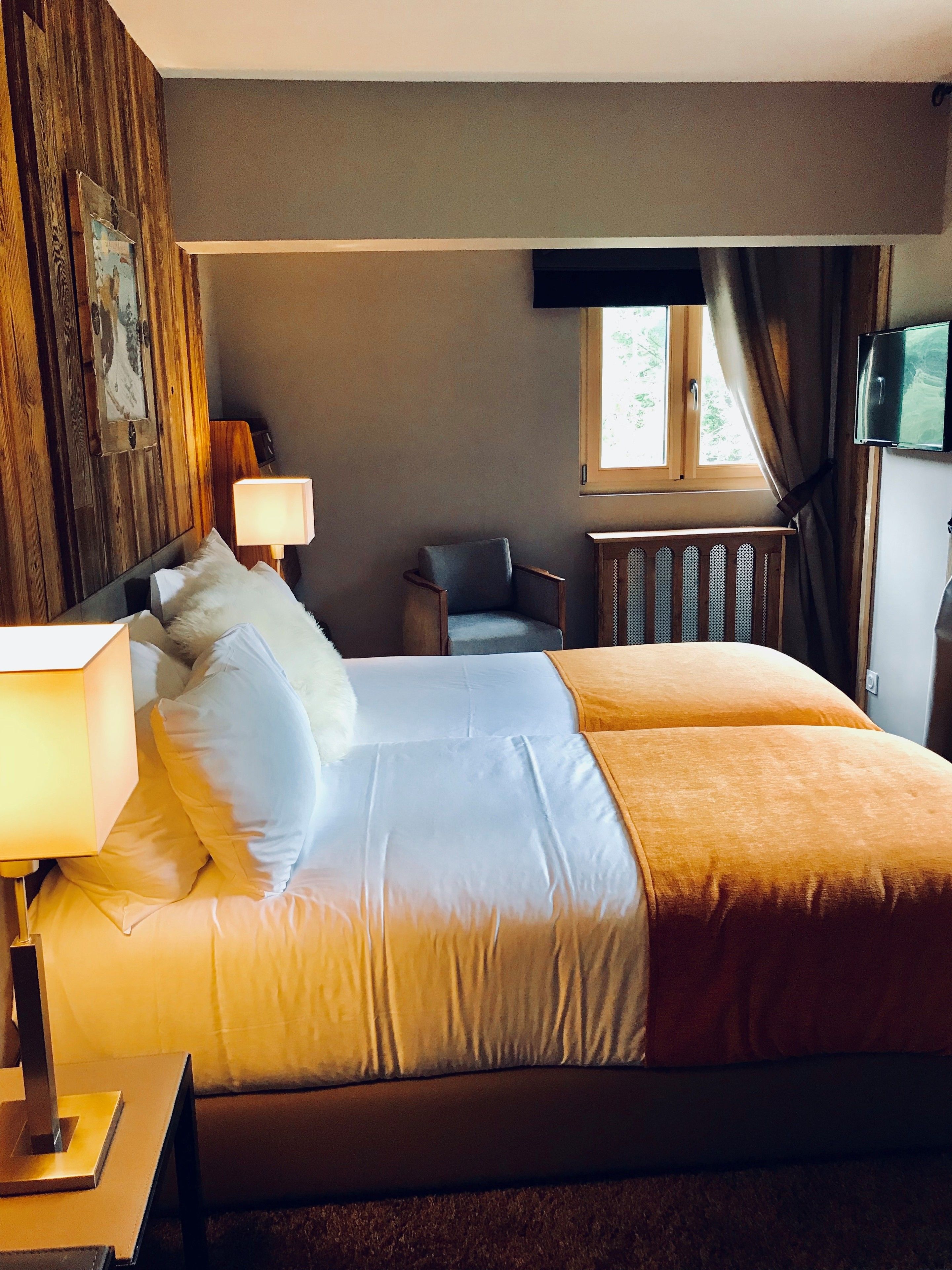 A hotel room with a large bed, a chair, a desk with a lamp, a television, and a window with curtains.
