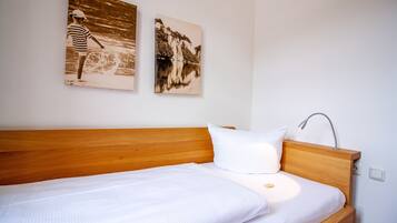 A neatly made bed with a wooden headboard, a white pillow, and a wall-mounted lamp. Two monochrome photographs are hung above the bed.