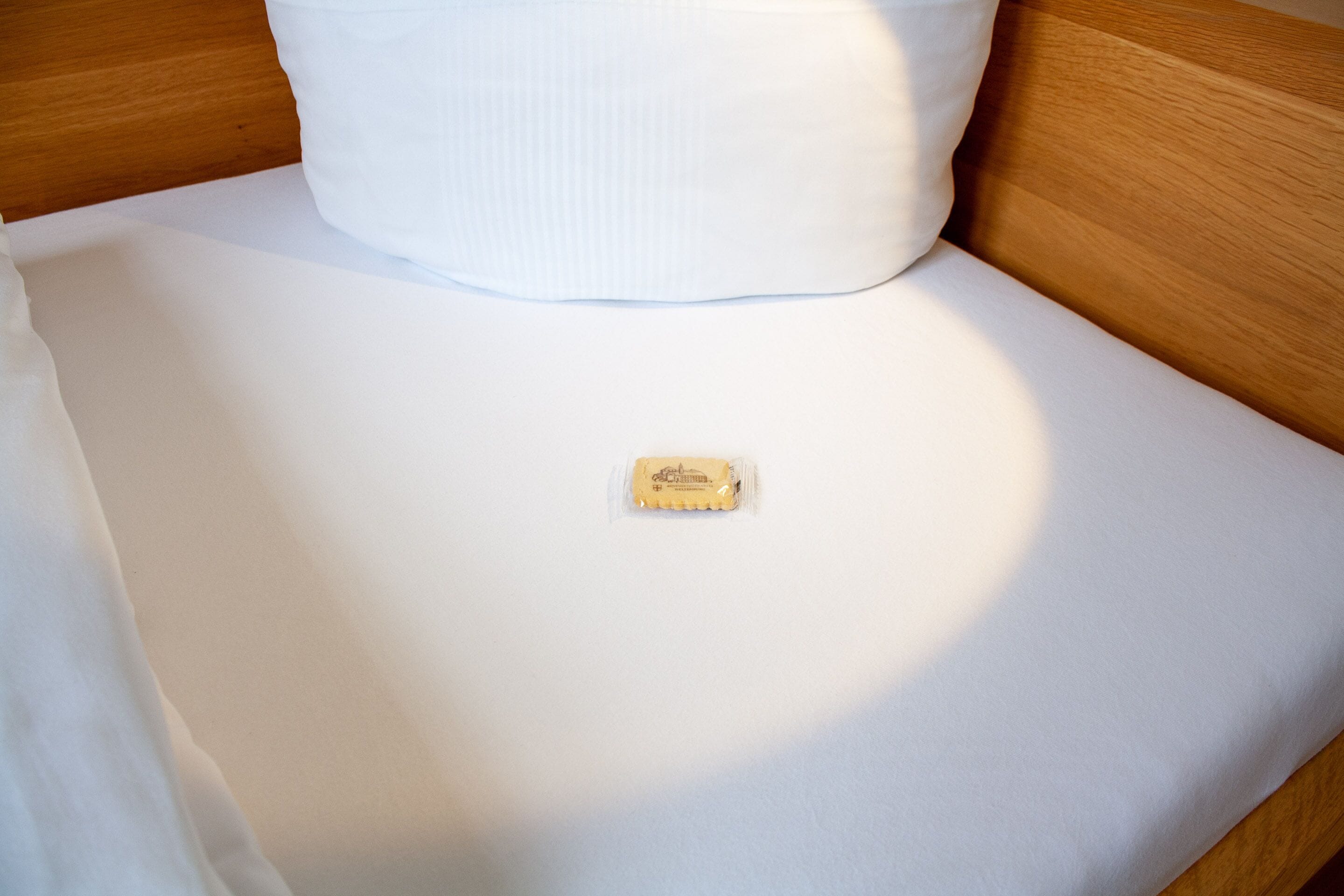 Una cama bien hecha con sábanas blancas y un pequeño paquete de plástico transparente sobre la cama.