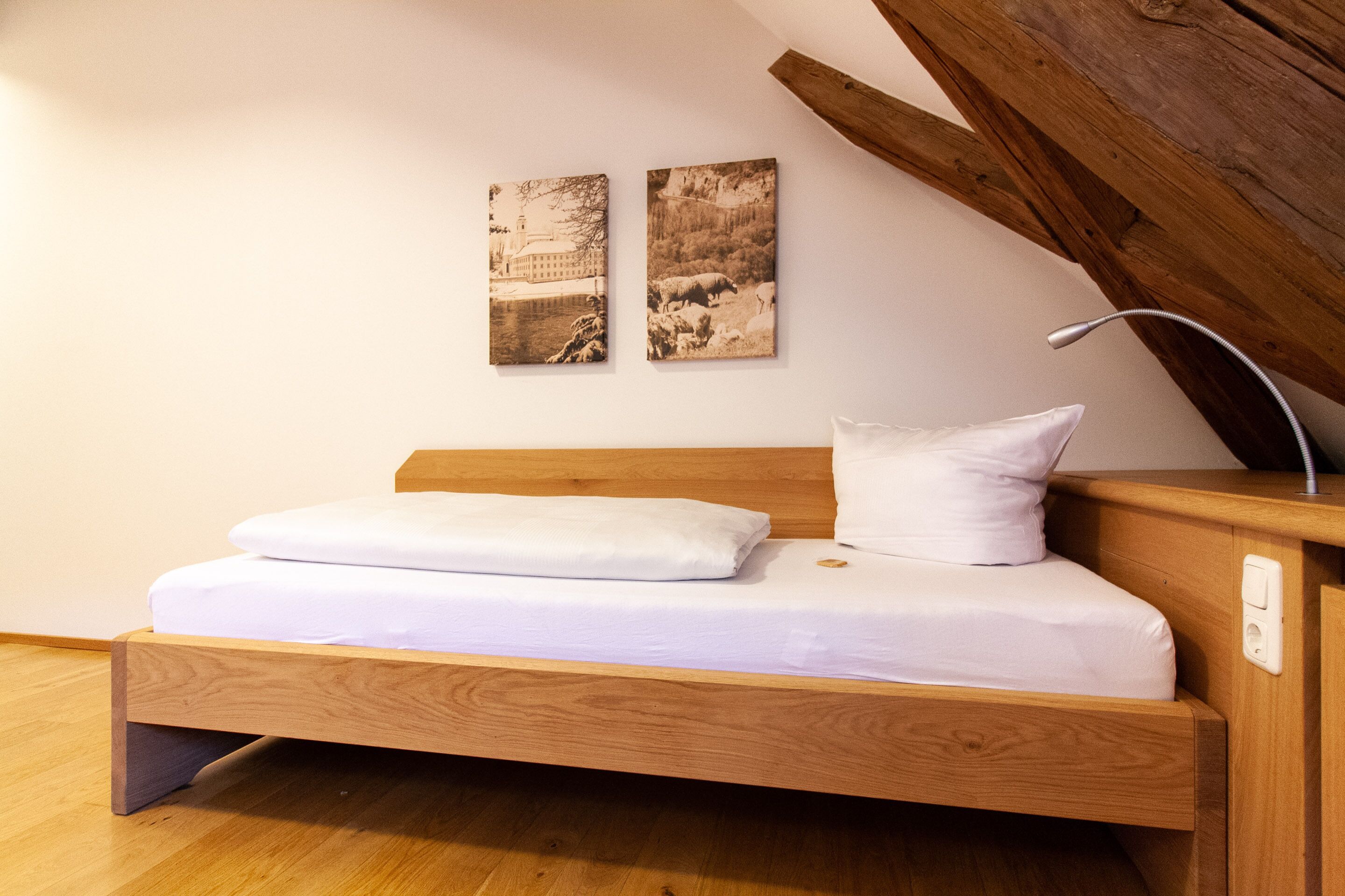 Ein Holzbett mit weißer Bettwäsche in einem Zimmer mit Holzbalken und zwei Landschaftsbildern an der Wand.