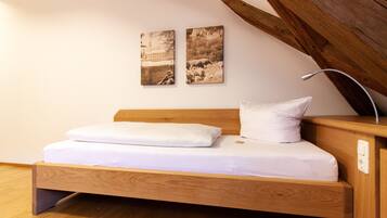 Ein Holzbett mit weißer Bettwäsche in einem Zimmer mit Holzbalken und zwei Landschaftsbildern an der Wand.