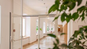 A hallway with glass doors, potted plants, and a tiled floor.