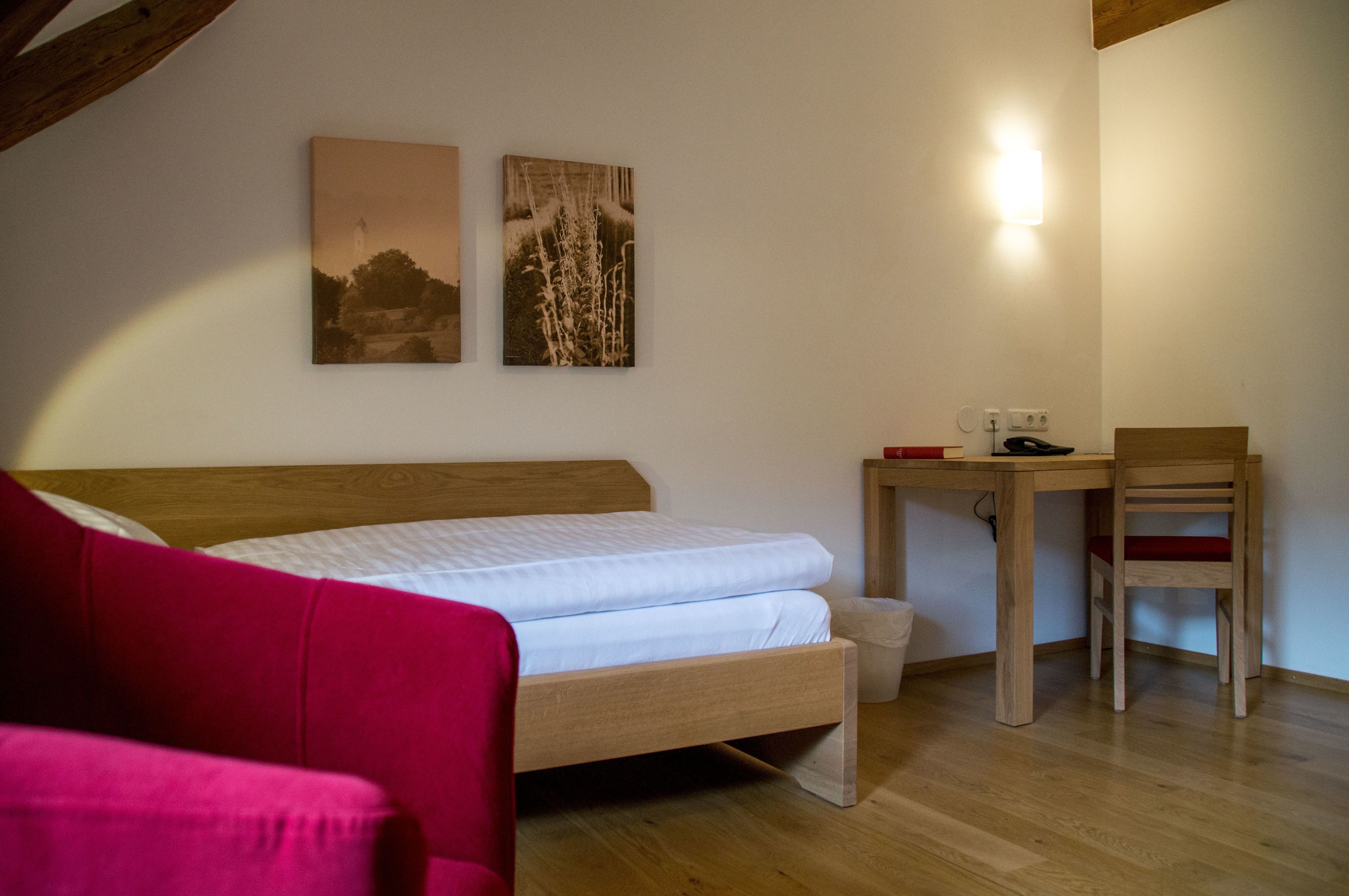 Un dormitorio con cama de madera, un escritorio pequeño, una silla y dos cuadros colgados.