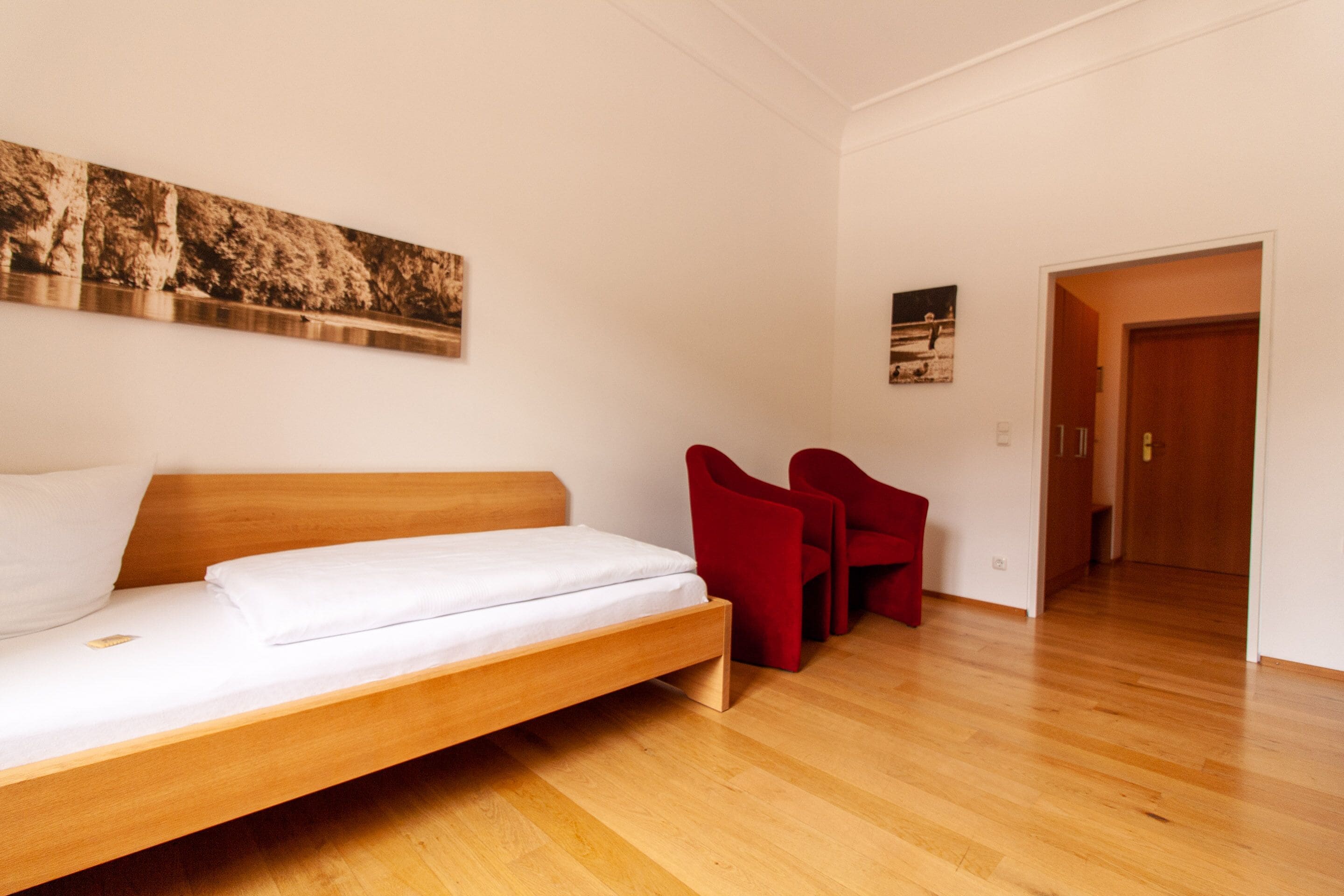 Une pièce avec un lit en bois, des chaises rouges et un plancher en bois.