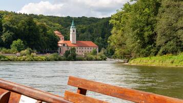A riverside view of a historic building with a tower, surrounded by lush greenery.