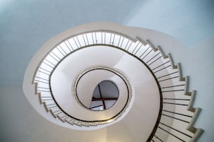 Escadaria em espiral com área central aberta e claraboia circular.